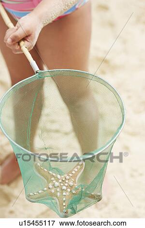 Stock Photo - Girl (7-9 years) holding starfish in net low section elevated view. Fotosearch