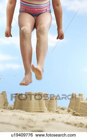 Girl (7-9 years) jumping on sand castle on beach low section View Large Photo Image Stock Photograph - Girl (7-9 years) jumping on sand castle on beach low section. Fotosearch
