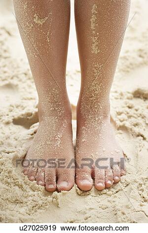 Stock Photo - Girl (7-9 years) standing on sandy beach low section. Fotosearch