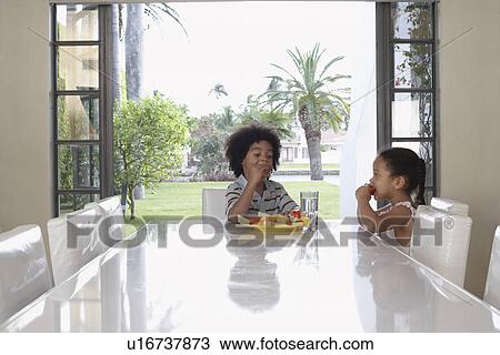 Girl and boy (5-6 years) eating at dining table View Large Photo Image Stock Image - Girl and boy (5-6 years) eating at dining table. Fotosearch