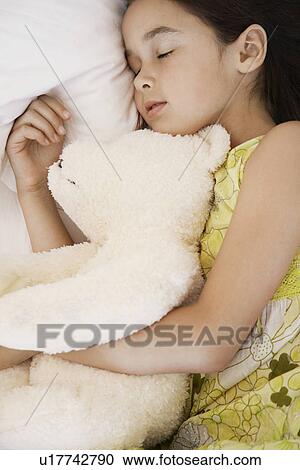 Stock Image - Girl cuddling teddy asleep on bed. Fotosearch
