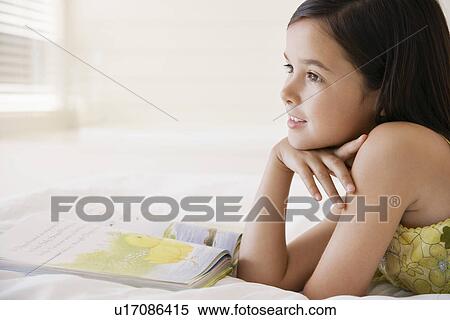 Girl daydreaming whilst reading book lying on bed head and shoulders View Large Photo Image Stock Photography - Girl daydreaming whilst reading book lying on bed head and shoulders. Fotosearch