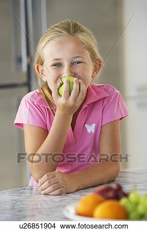 Girl eating apple in kitchen View Large Photo Image Picture - Girl eating apple in kitchen. Fotosearch