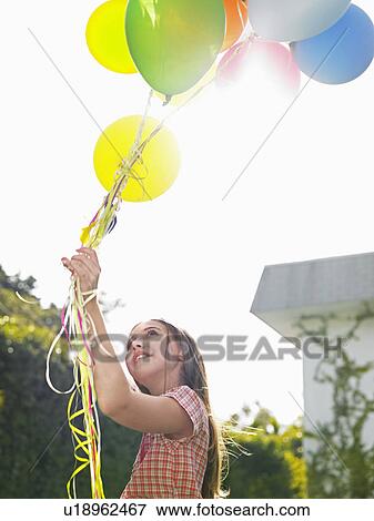 Stock Photo - Girl holding bunch of balloons looking up smilig. Fotosearch