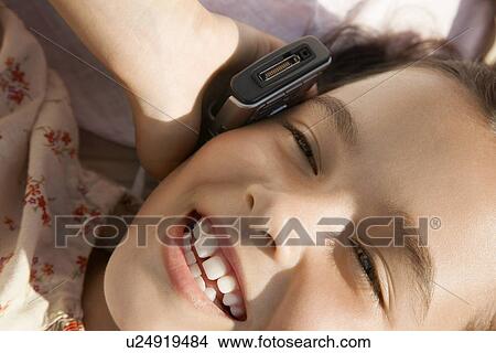 Girl lying down using mobile phone head and shoulders close up View Large Photo Image Picture - Girl lying down using mobile phone head and shoulders close up. Fotosearch
