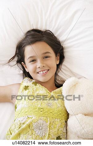 Picture - Girl lying on bed with teddy bear smiling half length. Fotosearch
