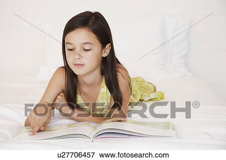 Stock Photo - Girl reading story book lying on bed. Fotosearch