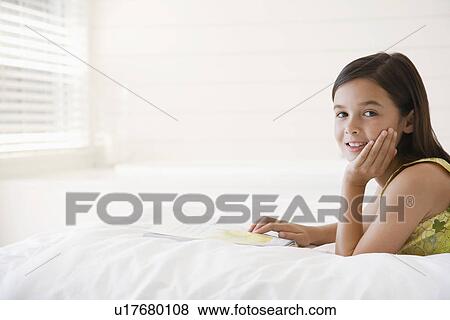 Stock Photo - Girl reading story book lying on stomach on bed head and shoulders. Fotosearch