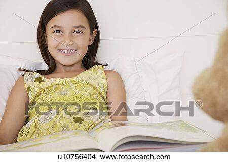Picture - Girl reading story to teddy bears sitting on bed half length. Fotosearch