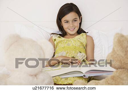 Stock Photograph - Girl reading story to teddy bears sitting on bed. Fotosearch