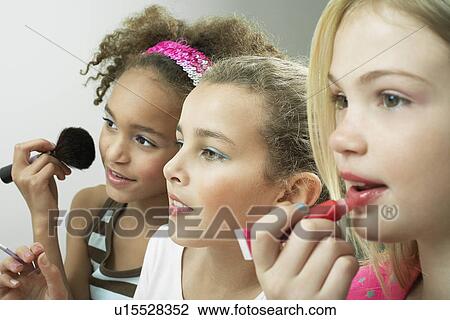 Stock Image - Girls standing side by side putting on make-up and lip gloss. Fotosearch
