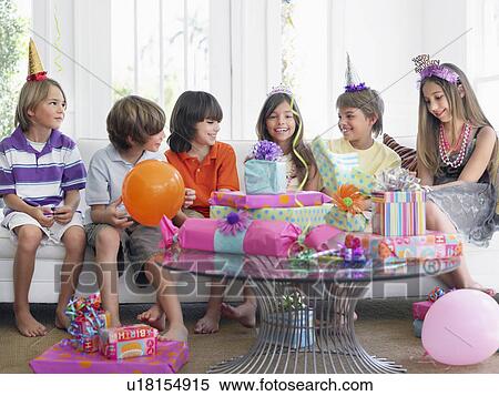 Stock Photography - Group of children (7-12) sitting on sofa at birthday party. Fotosearch