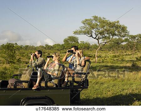 Stock Photography - Group of tourists on safari sitting in jeep looking through binoculars. Fotosearch