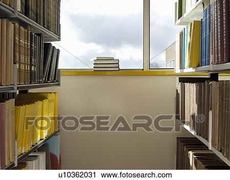 Stock Image - Library interior pile of books on windowsill. Fotosearch