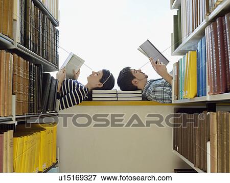 Stock Photo - Male and female student lying down on windowsill in library reading. Fotosearch