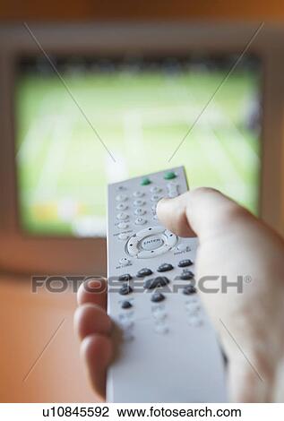 Stock Image - Man adjusting TV channel volume with remote control close-up of hand. Fotosearch