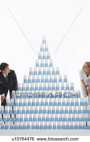 Stock Photograph - Man and woman admiring pyramid of stacked plastic cups against white background. Fotosearch