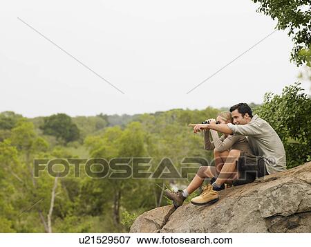 Man and woman sitting on rock looking at view man pointing View Large Photo Image Stock Photo - Man and woman sitting on rock looking at view man pointing. Fotosearch