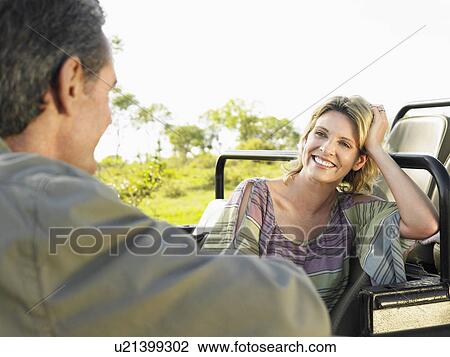 Stock Image - Man and woman talking woman leaning with elbow on jeep focus on woman. Fotosearch