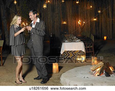 Stock Photograph - Man and woman toasting at outdoor nightclub near bonfire night. Fotosearch
