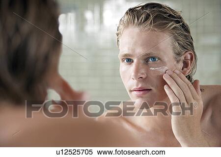 Stock Photography - Man applying facial cream in front of mirror. Fotosearch