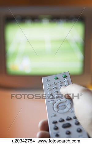 Picture - Man changing TV channel with remote control close-up on hand. Fotosearch