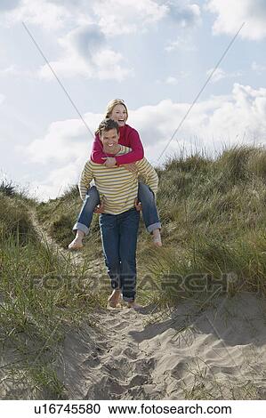 Stock Image - Man giving woman piggy back on sand dunes. Fotosearch
