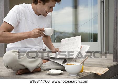 Stock Photograph - Man having breakfast and reading papers on porch. Fotosearch