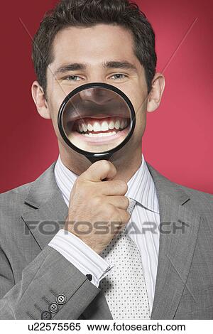 Man holding magnifying glass to smiling mouth against red background View Large Photo Image Stock Photography - Man holding magnifying glass to smiling mouth against red background. Fotosearch