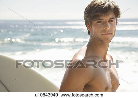 Stock Photo - Man holding surfboard by ocean head and shoulders. Fotosearch