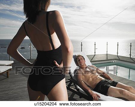Man on a deck chair looking up at woman at pool by ocean View Large Photo Image Picture - Man on a deck chair looking up at woman at pool by ocean. Fotosearch