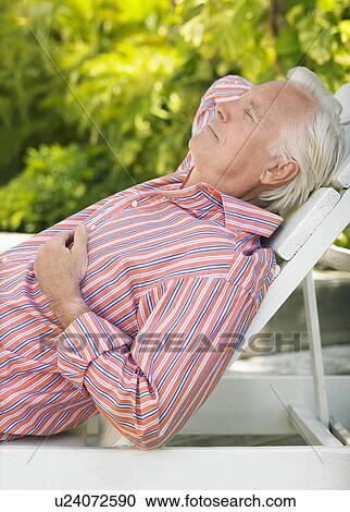 Stock Image - Man reclining on lounge chair outdoors side view. Fotosearch