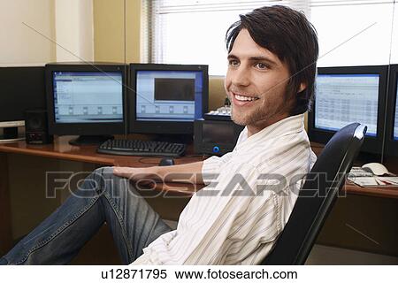 Stock Photography - Man sitting at desk in front of computers.. Fotosearch