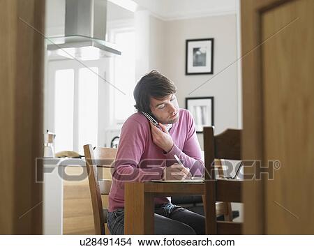 Man sitting in kitchen using phone View Large Photo Image Picture - Man sitting in kitchen using phone. Fotosearch