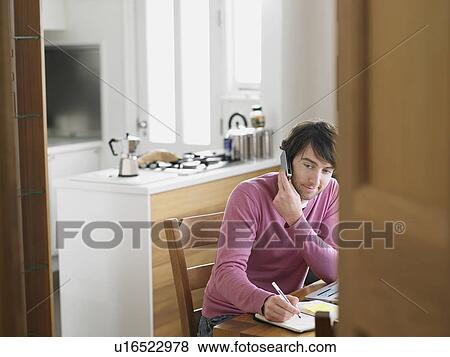Man sitting in kitchen using phone elevated view View Large Photo Image Stock Photo - Man sitting in kitchen using phone elevated view. Fotosearch