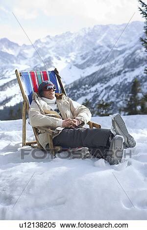Stock Photography - Man sitting on deckchair in snowy mountains. Fotosearch