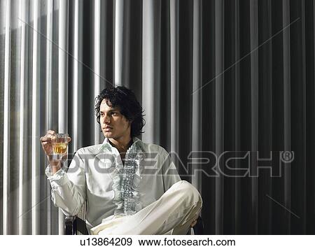 Stock Photo - Man sitting with alcoholic drink in front of curtains. Fotosearch