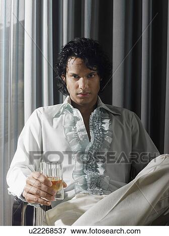 Stock Photo - Man sitting with alcoholic drink in front of curtains. Fotosearch