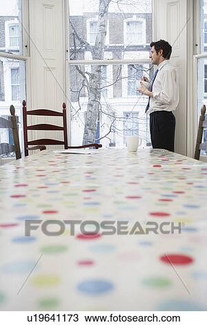 Stock Image - Man standing at window in dining room. Fotosearch
