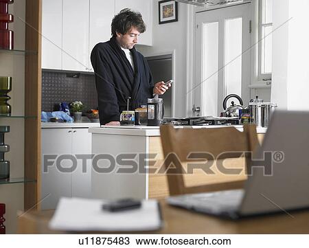 Man standing in kitchen text messaging laptop on table in foreground View Large Photo Image Stock Image - Man standing in kitchen text messaging laptop on table in foreground. Fotosearch