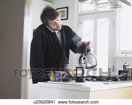 Man standing in kitchen using phone pouring water into coffee plunger View Large Photo Image Stock Image - Man standing in kitchen using phone pouring water into coffee plunger. Fotosearch