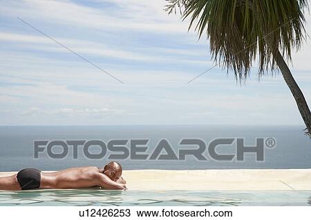 Man sunbathing at edge of pool ocean in background View Large Photo Image Stock Image - Man sunbathing at edge of pool ocean in background. Fotosearch