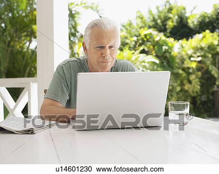 Stock Image - Man using laptop at verandah table. Fotosearch