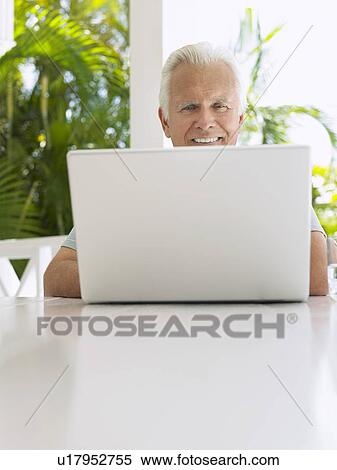 Stock Photography - Man using laptop at verandah table. Fotosearch