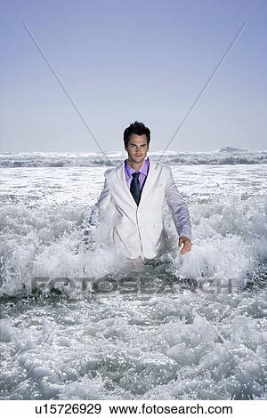 Stock Photo - Man walking in sea being washed by waves portrait. Fotosearch