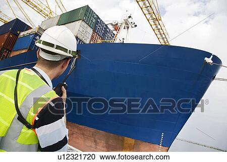 Man wearing hard hat using walkie-talkie at container terminal back view View Large Photo Image Stock Image - Man wearing hard hat using walkie-talkie at container terminal back view. Fotosearch