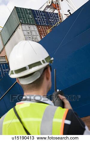 Man wearing hard hat using walkie-talkie at container terminal back view View Large Photo Image Stock Image - Man wearing hard hat using walkie-talkie at container terminal back view. Fotosearch