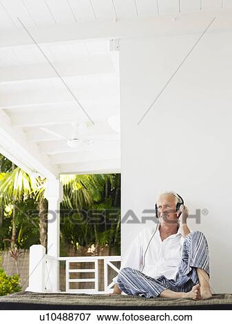 Stock Photo - Man wearing headphones sitting on verandah. Fotosearch