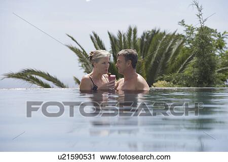 Stock Image - Mature couple drinking daiquiri in outdoor pool. Fotosearch