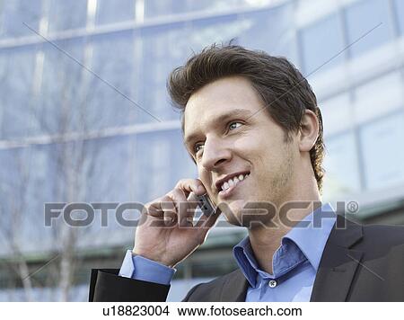 Mid adult businessman in front of office building using mobile phone View Large Photo Image Picture - Mid adult businessman in front of office building using mobile phone. Fotosearch